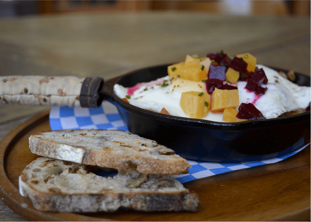 an egg dish topped with pickeled vegetables and a side of walnut bread toast 