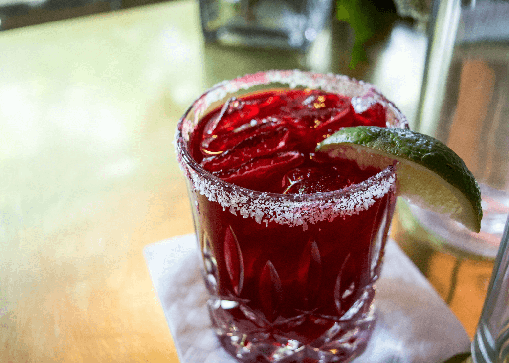 a red cocktail with a rim and lime wedge